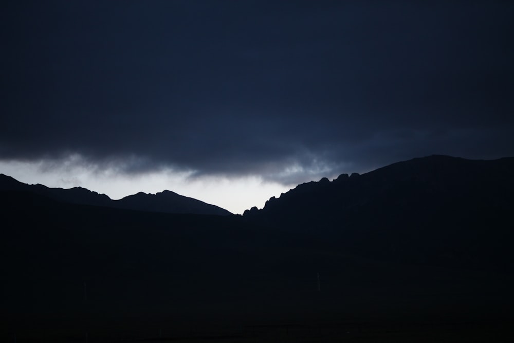 silhouette of mountain under cloudy sky during night time