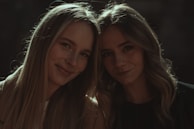 Two women sharing a quiet moment, their skin radiant under soft white and gold lighting.