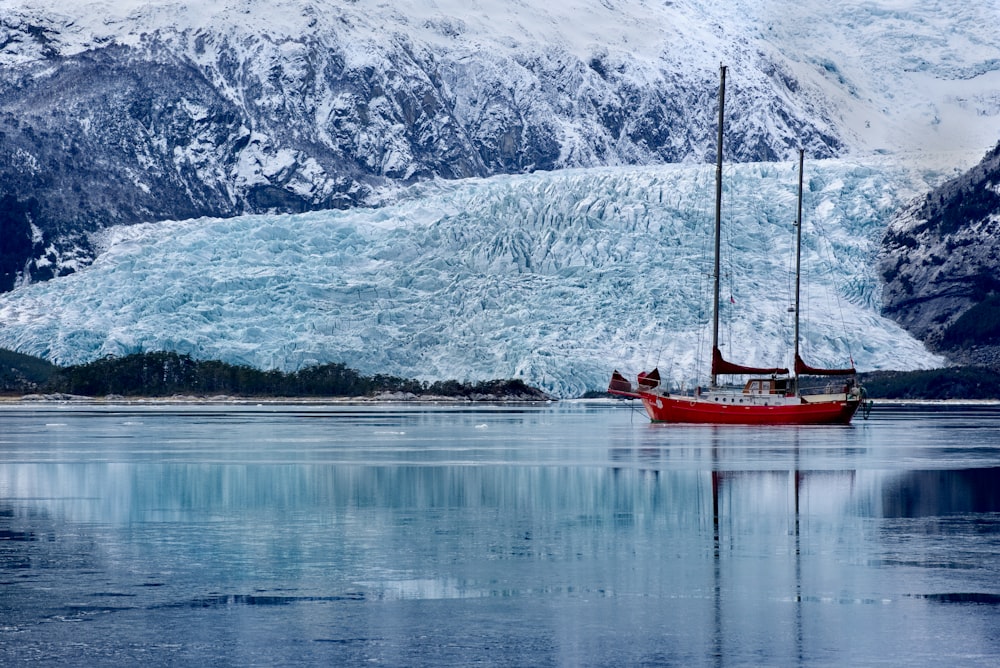 red boat on lake near snow covered mountain during daytime