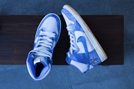 A pair of high-top sneakers with a blue and white color scheme are placed on a wooden surface. The sneakers have a stylish design with a star logo on the side and light brown soles.