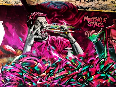 A vibrant graffiti mural featuring a stylized figure with wide eyes and open mouth, wearing a headband and holding a spray paint can. Dynamic colors and abstract elements swirl around the figure. The words 'Meeting of Styles' are prominently displayed, suggesting an artistic collaboration or event.