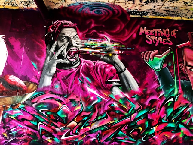 A vibrant graffiti mural featuring a stylized figure with wide eyes and open mouth, wearing a headband and holding a spray paint can. Dynamic colors and abstract elements swirl around the figure. The words 'Meeting of Styles' are prominently displayed, suggesting an artistic collaboration or event.