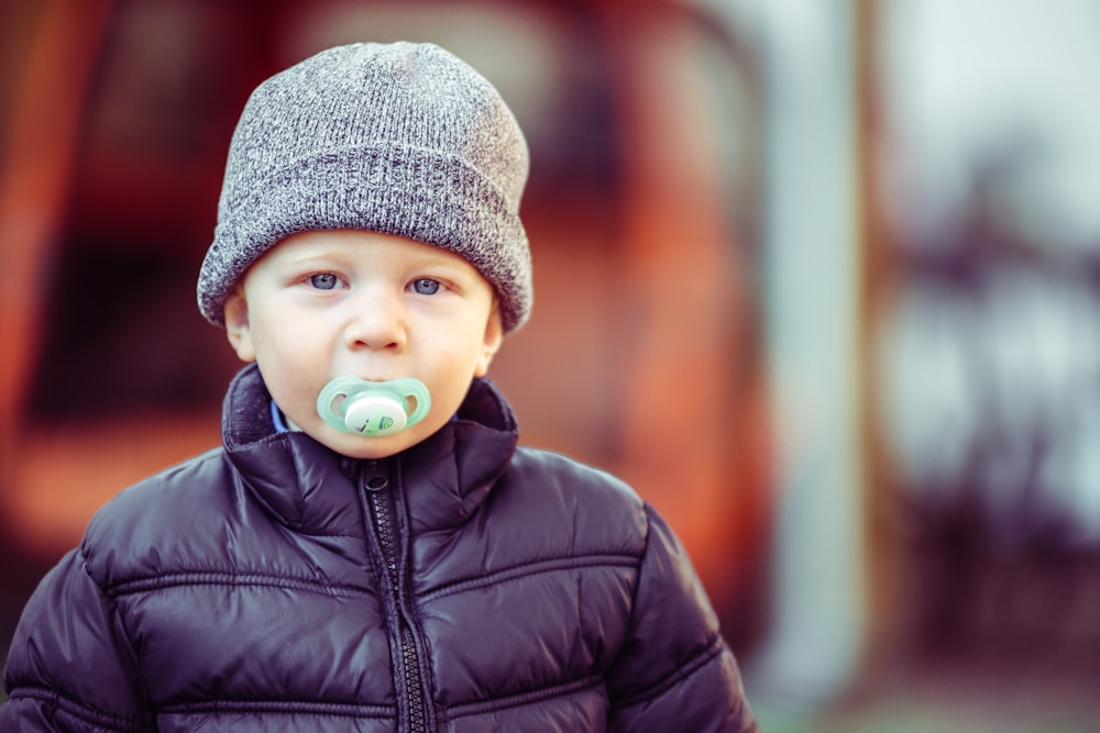 Foto Bebé con gorro de punto gris y chaqueta de cuero negro con chupete  azul en la boca – Imagen Gris gratis en Unsplash
