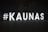 Large illuminated letters spell out #KAUNAS against a dark background, standing on an outdoor pavement area. The letters are evenly spaced and brightly lit, creating a stark contrast with the night around them.