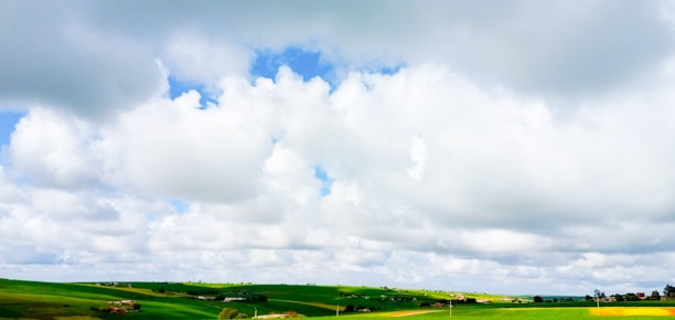 Spacious countryside farmhouse surrounded by rolling green fields under a bright blue sky.
