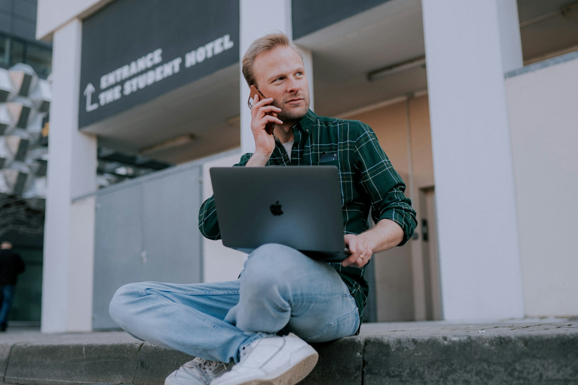 young man sitting, working remote with iphone and macbook pro