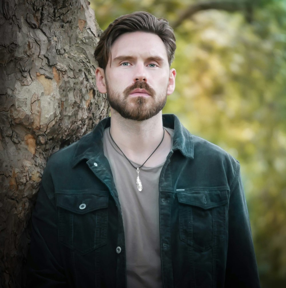 man in black zip up jacket standing beside brown tree during daytime