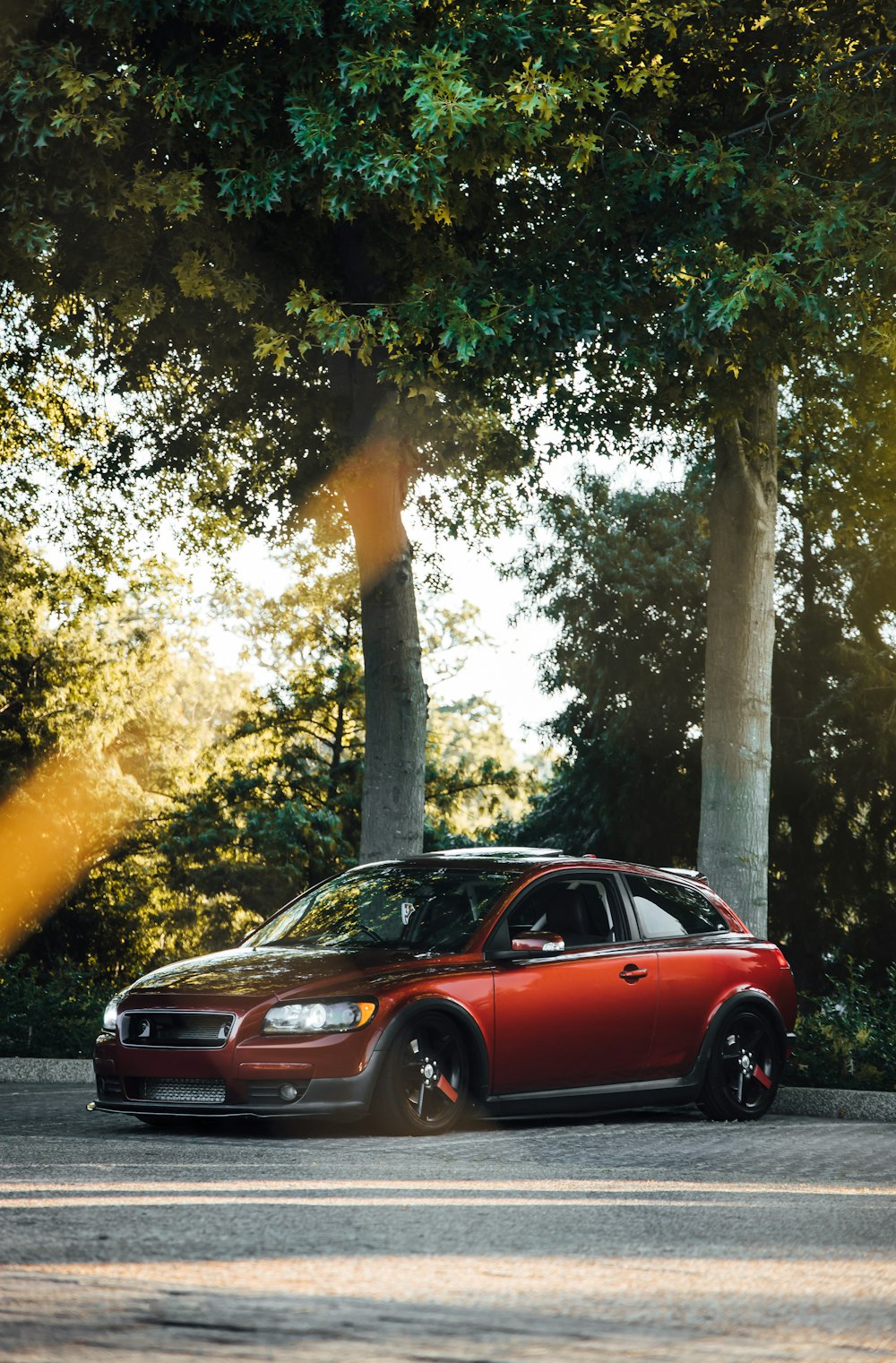 red sedan parked near green trees during daytime