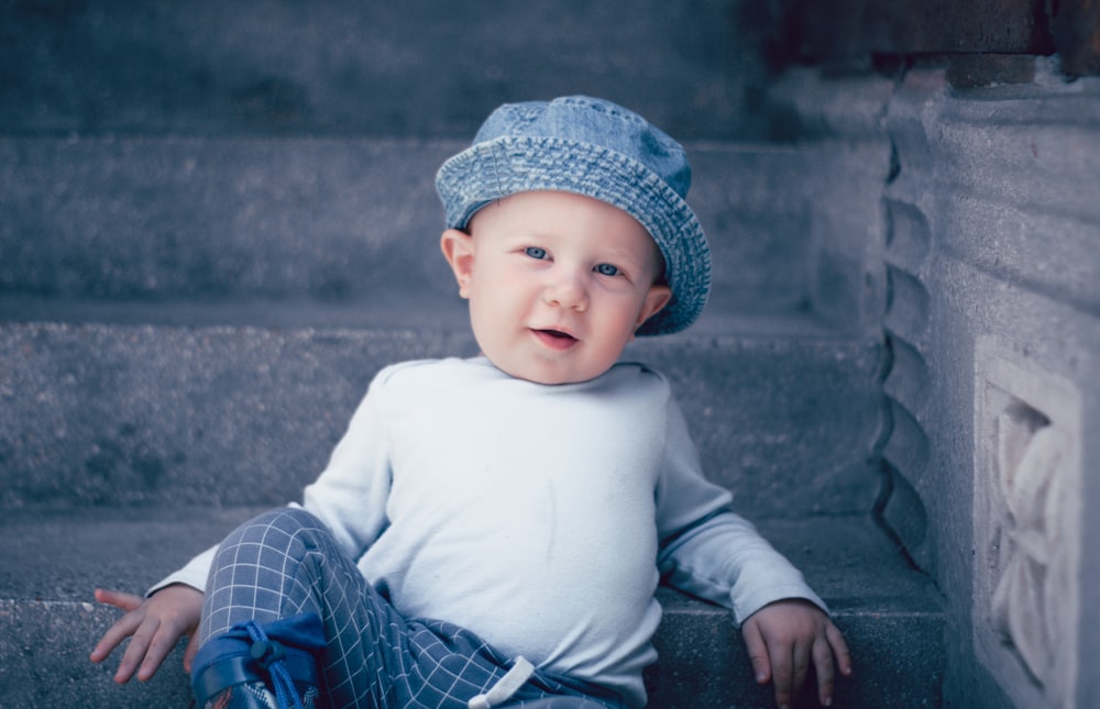 baby in white long sleeve shirt and blue and white plaid pants sitting on gray concrete