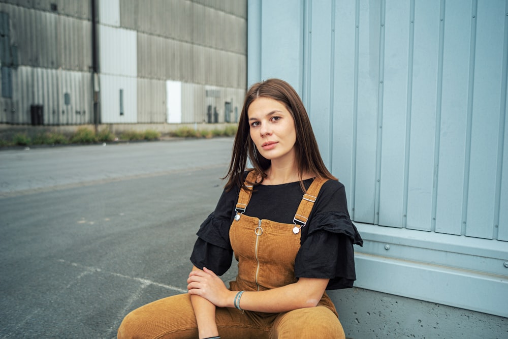 woman in black long sleeve shirt and brown pants sitting on gray concrete floor