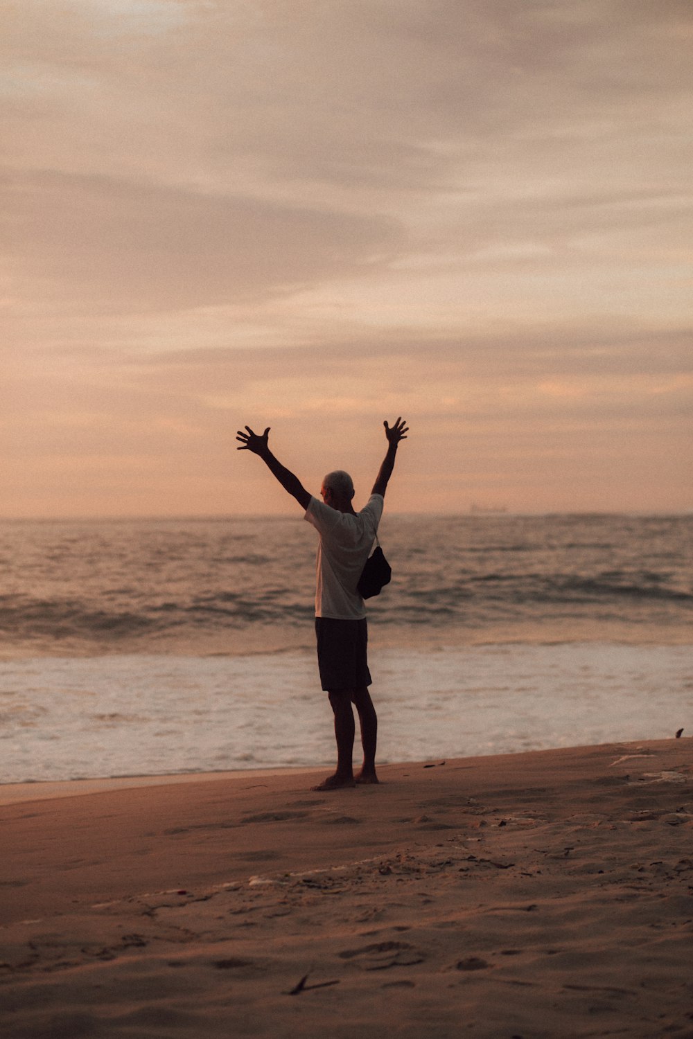 man in white shirt and black shorts standing on seashore during sunset