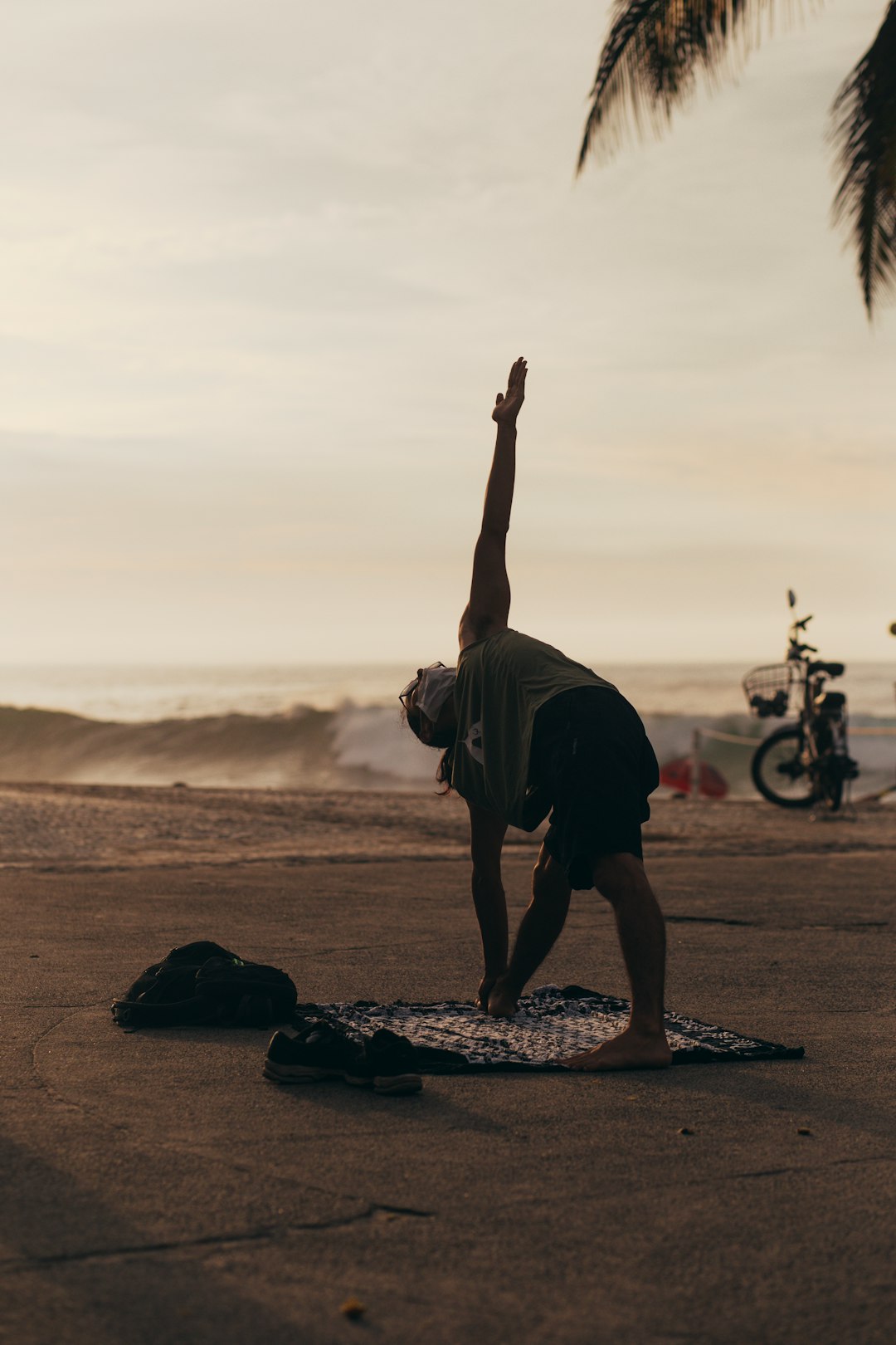 man in black t-shirt and black shorts doing yoga on brown sand during sunset