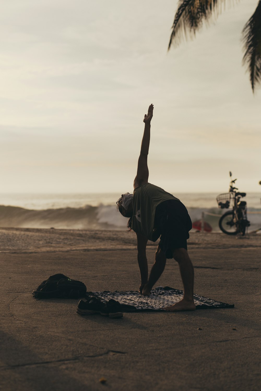homme en t-shirt noir et short noir faisant du yoga sur le sable brun au coucher du soleil
