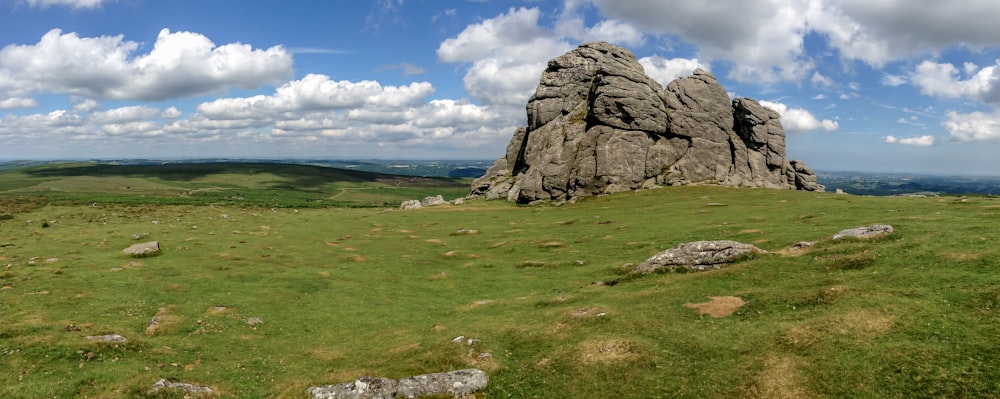 gray rock formation on green grass field under blue and white sunny cloudy sky during daytime