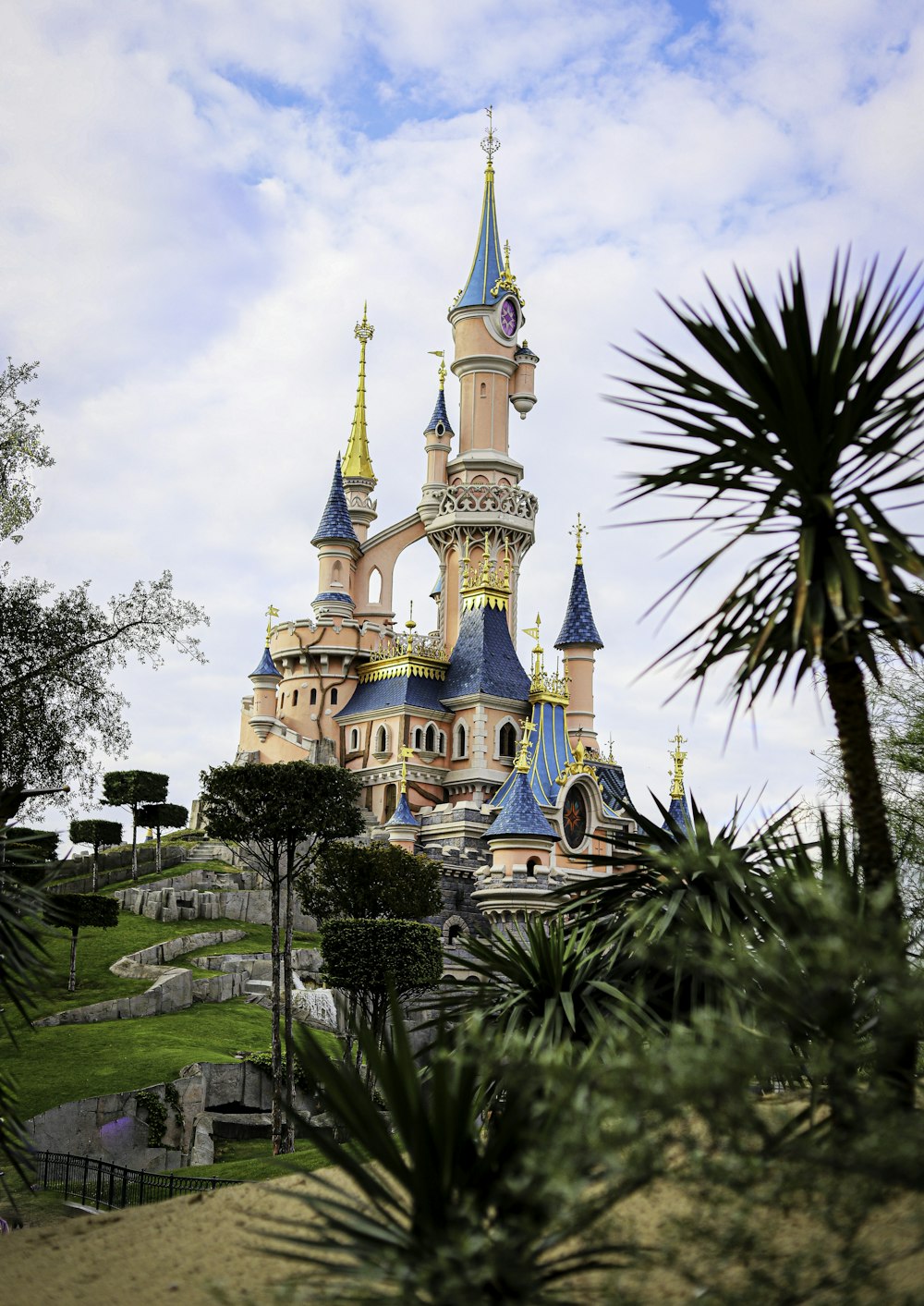 white and blue castle surrounded by green trees under white clouds and blue sky during daytime