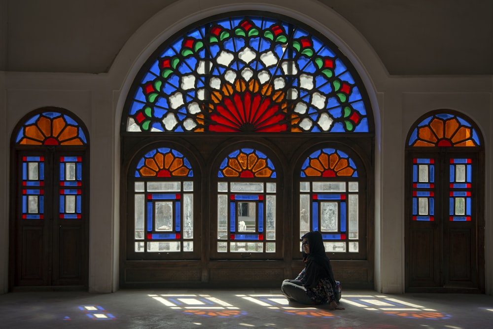 woman in black dress standing in front of blue red and green floral glass window