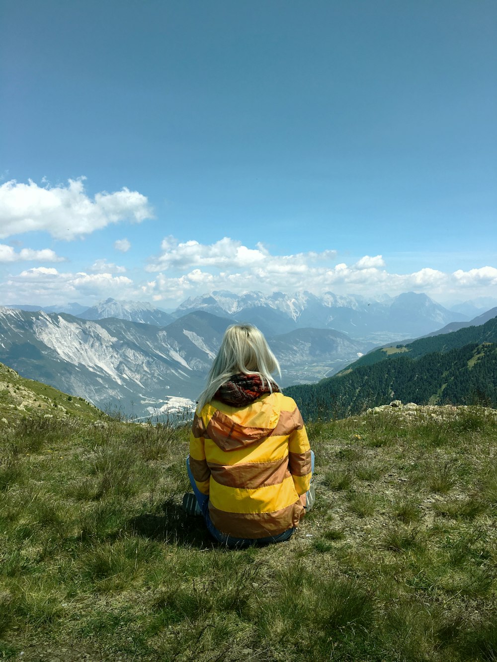 person in yellow and gray hoodie sitting on green grass field during daytime