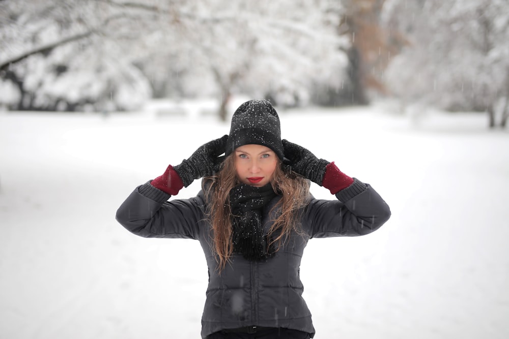 黒いジャケットと黒いニット帽をかぶった女性が、昼間、雪に覆われた地面に立つ