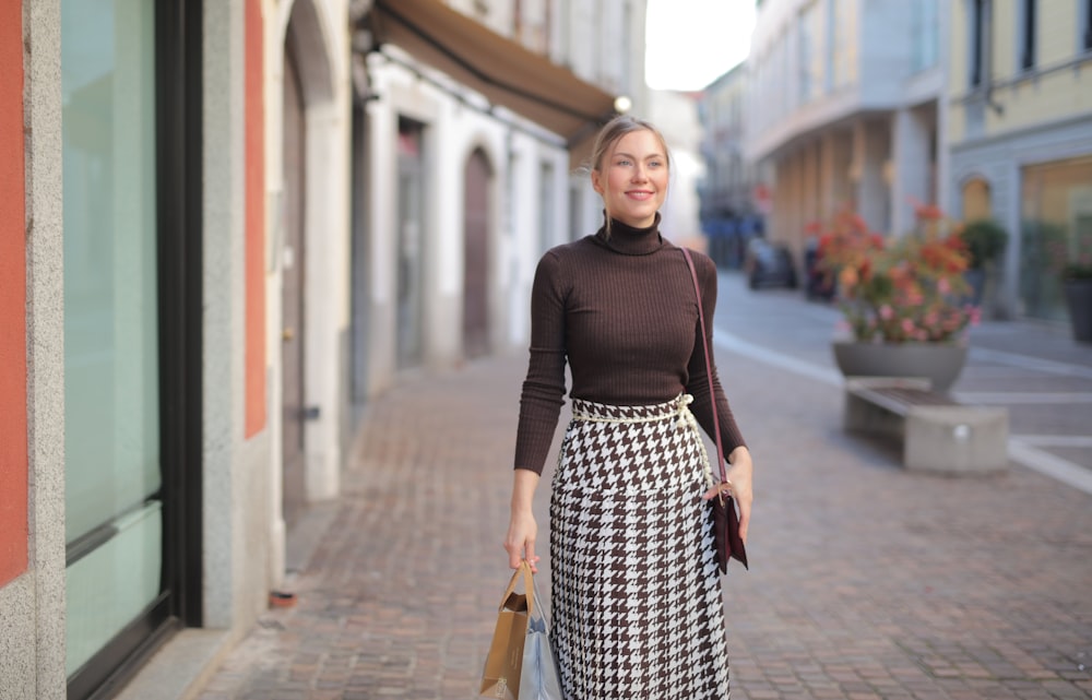 Femme en chemise à manches longues noire et jupe à pois noir et blanc debout sur le trottoir