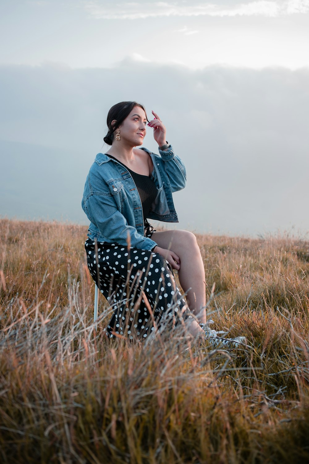 woman in blue denim jacket and black and white polka dots pants sitting on brown grass