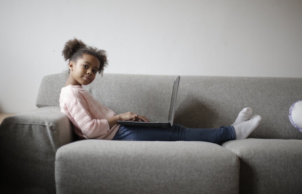 girl in pink long sleeve shirt and black pants sitting on gray couch