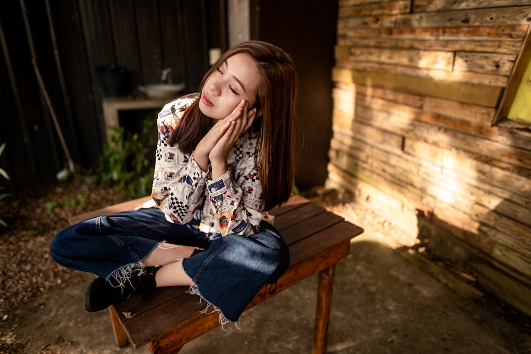 woman in white and black floral long sleeve shirt and blue denim jeans sitting on brown