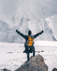 man in black jacket and yellow backpack standing on rock formation during daytime