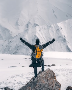 man in black jacket and yellow backpack standing on rock formation during daytime