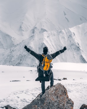 man in black jacket and yellow backpack standing on rock formation during daytime