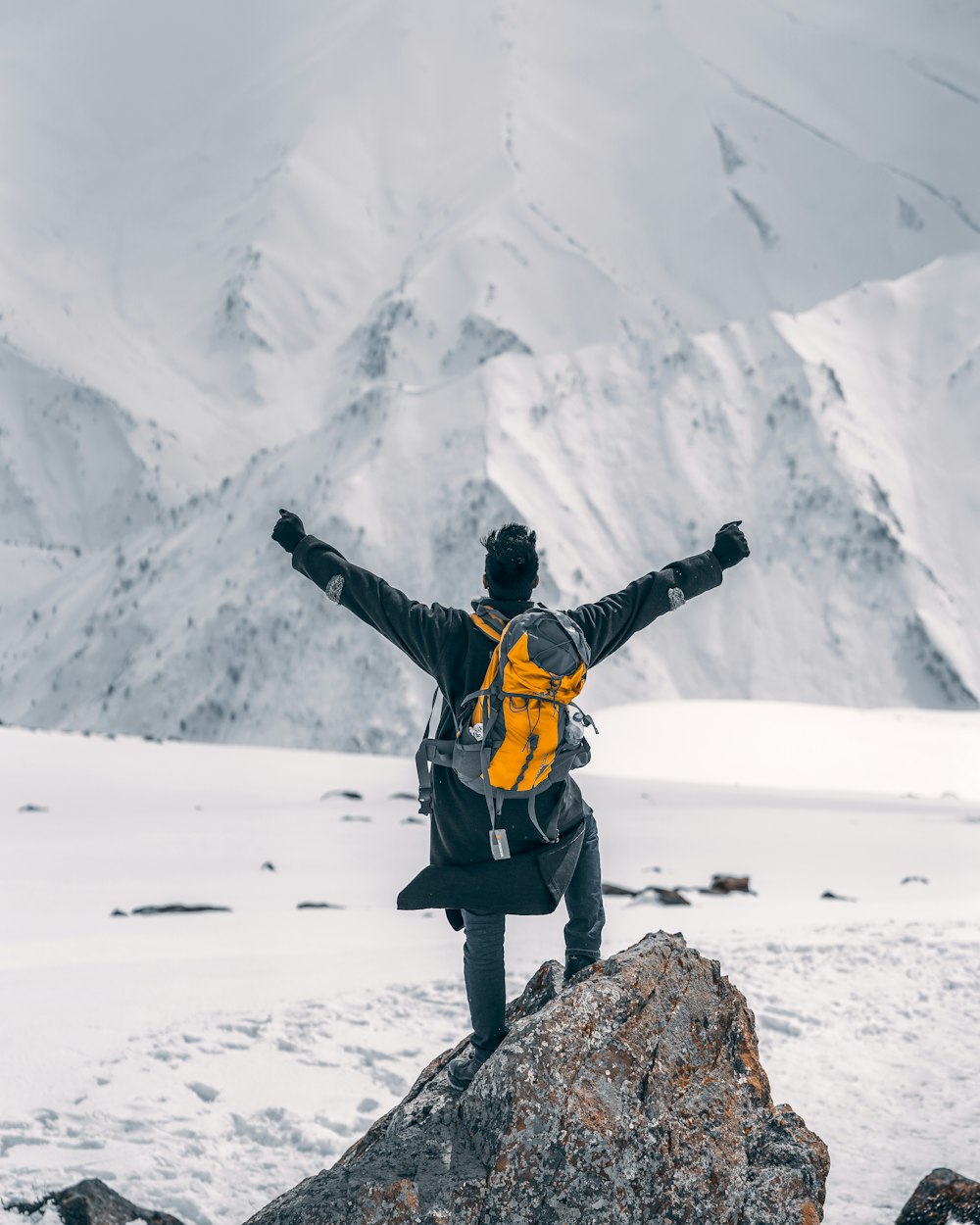 man in black jacket and yellow backpack standing on rock formation during daytime