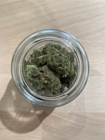 A small glass jar filled with assorted cannabis seeds on a rustic table.