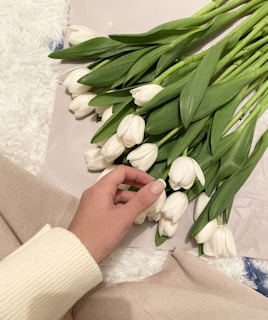 Close-up of a gentle hand placing flowers on a memorial table with white and dark orange tones.
