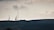 Telecommunication towers are silhouetted against a cloudy sky, standing on a hilly terrain covered with dark vegetation. The scene is calm yet somewhat imposing, with an overcast atmosphere.