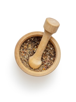 A wooden mortar filled with a variety of crushed spices, accompanied by a matching pestle resting inside. The spices are multi-colored, including shades of brown, yellow, and red, creating a visually appealing texture.