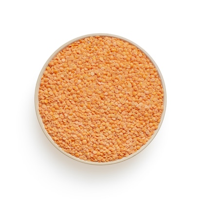 A circular bowl filled to the brim with small, orange-red lentils against a plain white background.