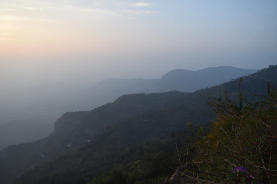 A serene mountain landscape with travelers enjoying a peaceful sunset overlooking lush green hills.