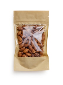 A brown paper bag with a transparent window displaying a collection of whole almonds. The packaging is simple and minimalistic, focusing on the natural appearance of the almonds inside.