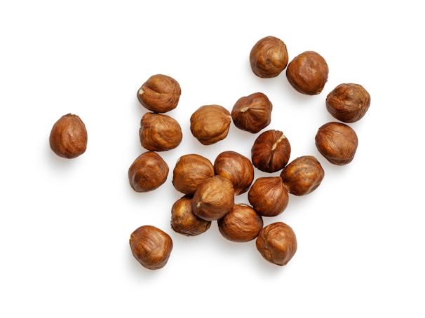 A cluster of hazelnuts scattered on a white background, each nut displaying a rich, brown color with a textured surface.
