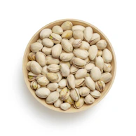 Hand selecting premium pistachios from a wooden bowl in a cozy market setting.