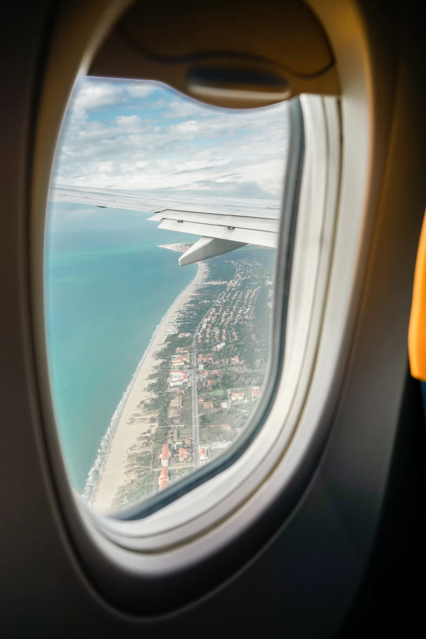View through an airplane passenger window of the wing over a coastline and blue ocean far below