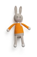 A crocheted stuffed bunny with long ears, wearing an orange and white outfit. The bunny has a neutral expression and a ribbon tied around its neck.