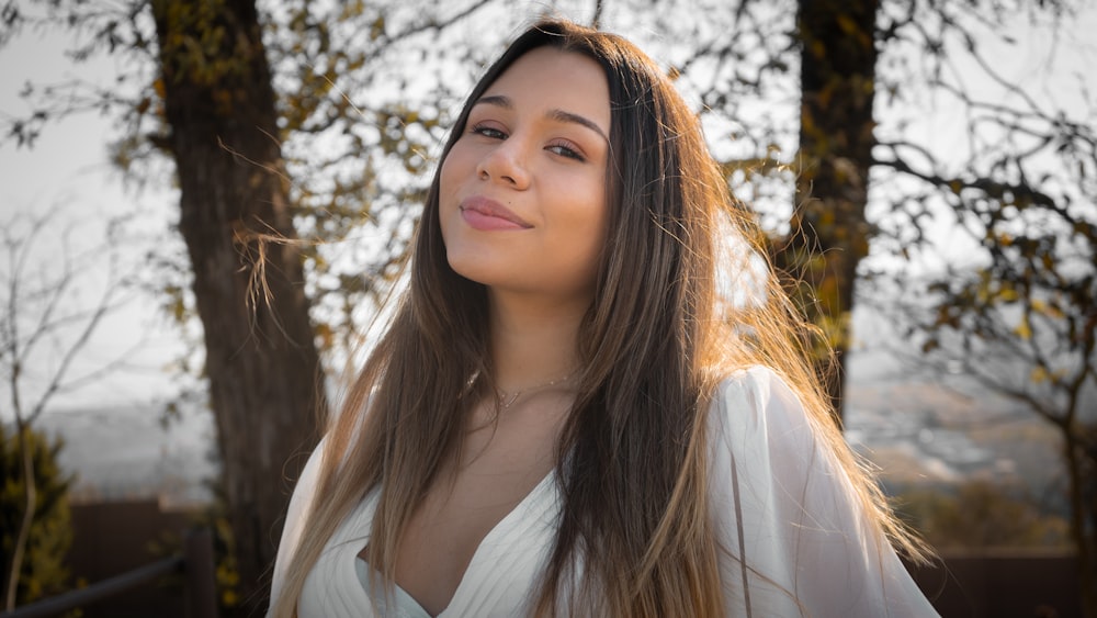 woman in white long sleeve shirt standing near brown tree during daytime