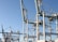 Massive industrial cranes dominate a port scene, with complex metal structures and machinery visible against a clear blue sky. These cranes are positioned above shipping containers and are likely used for loading and unloading cargo from ships.