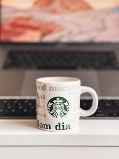 Close-up of a coffee mug featuring a Trump slogan, sitting on a desk next to a laptop and a small American flag