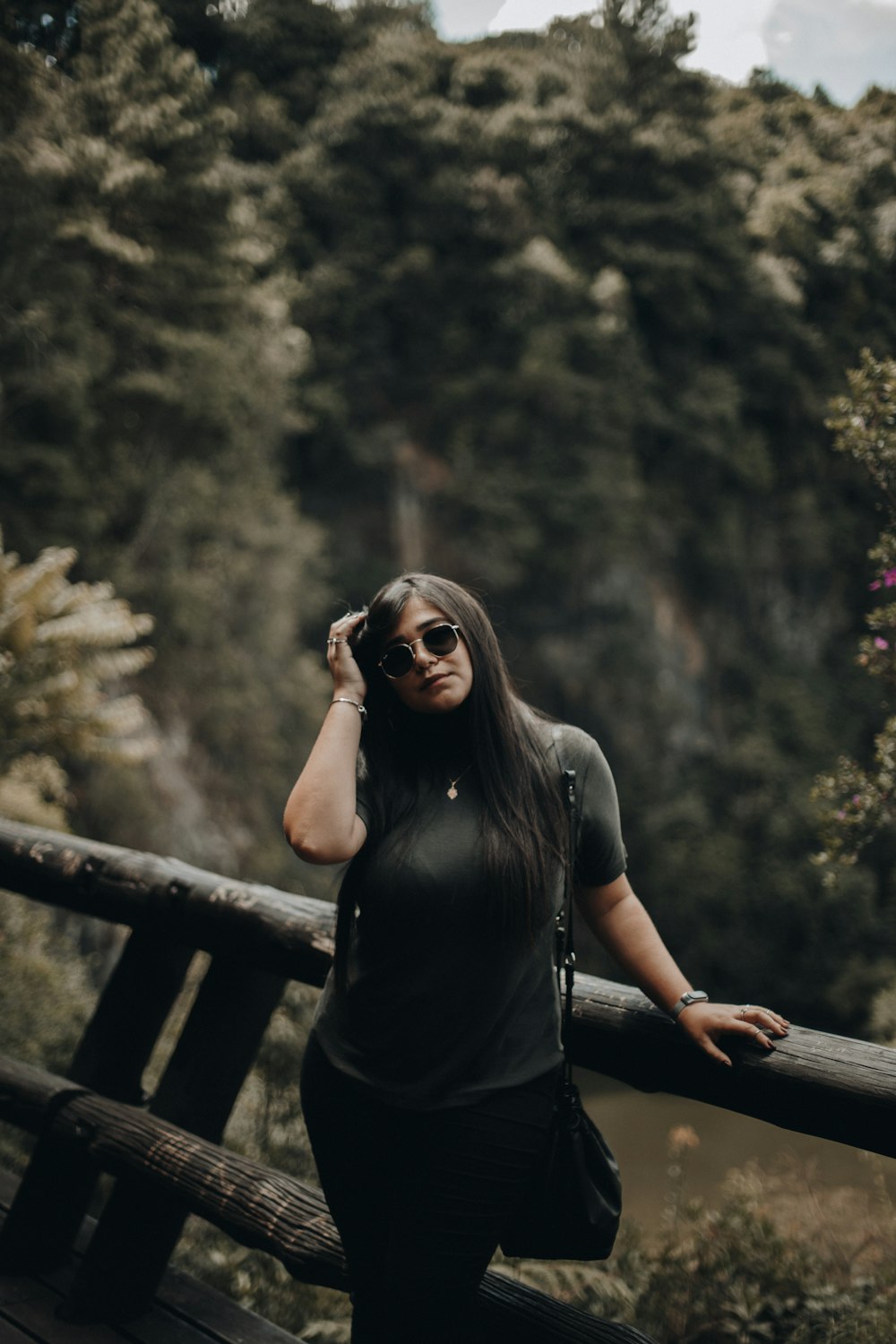 woman in black t-shirt and black sunglasses sitting on brown wooden fence during daytime