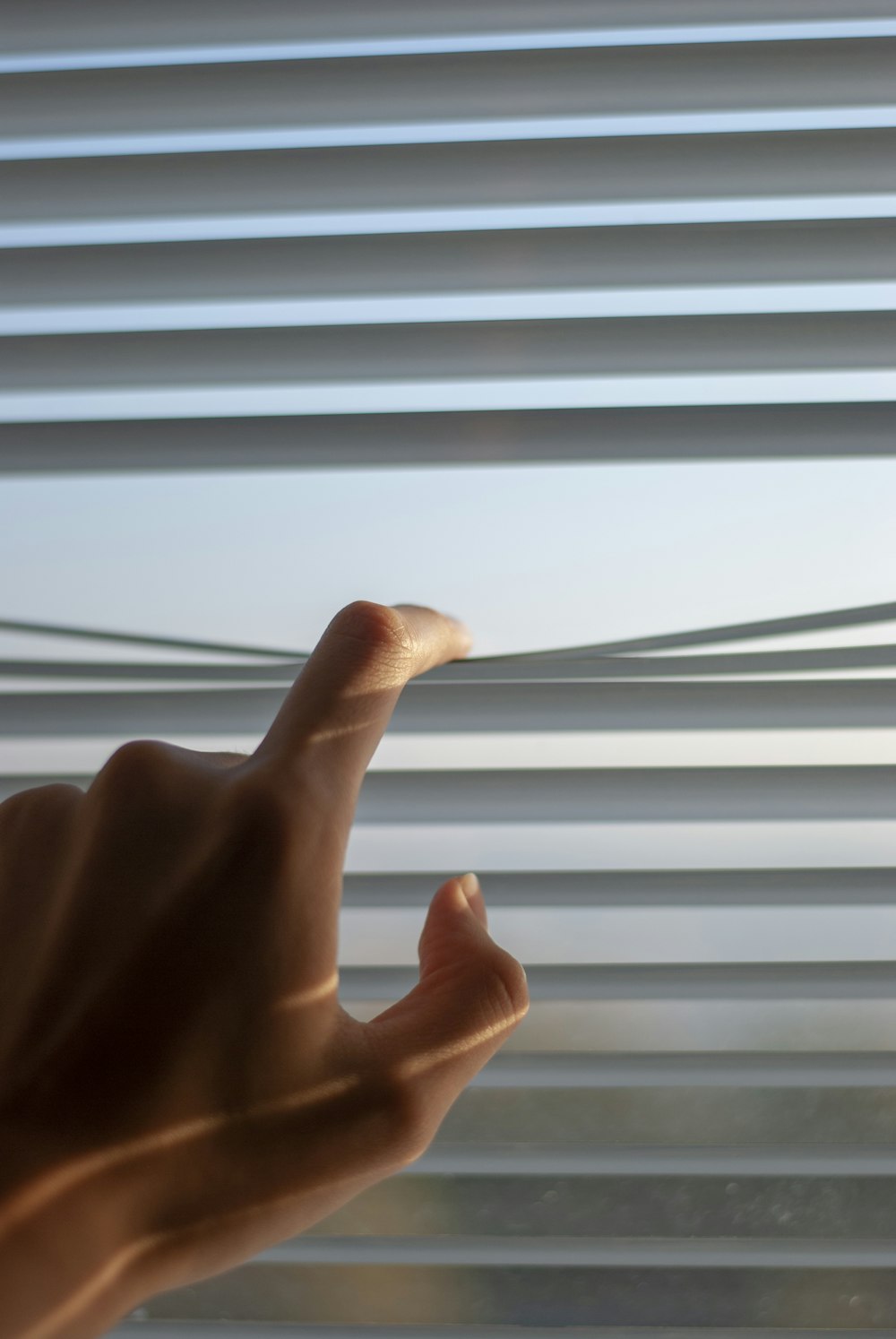 persons hand near white window blinds