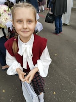 A young girl proudly holding a school bag donated by habby, standing in front of a modest home with a hopeful expression.