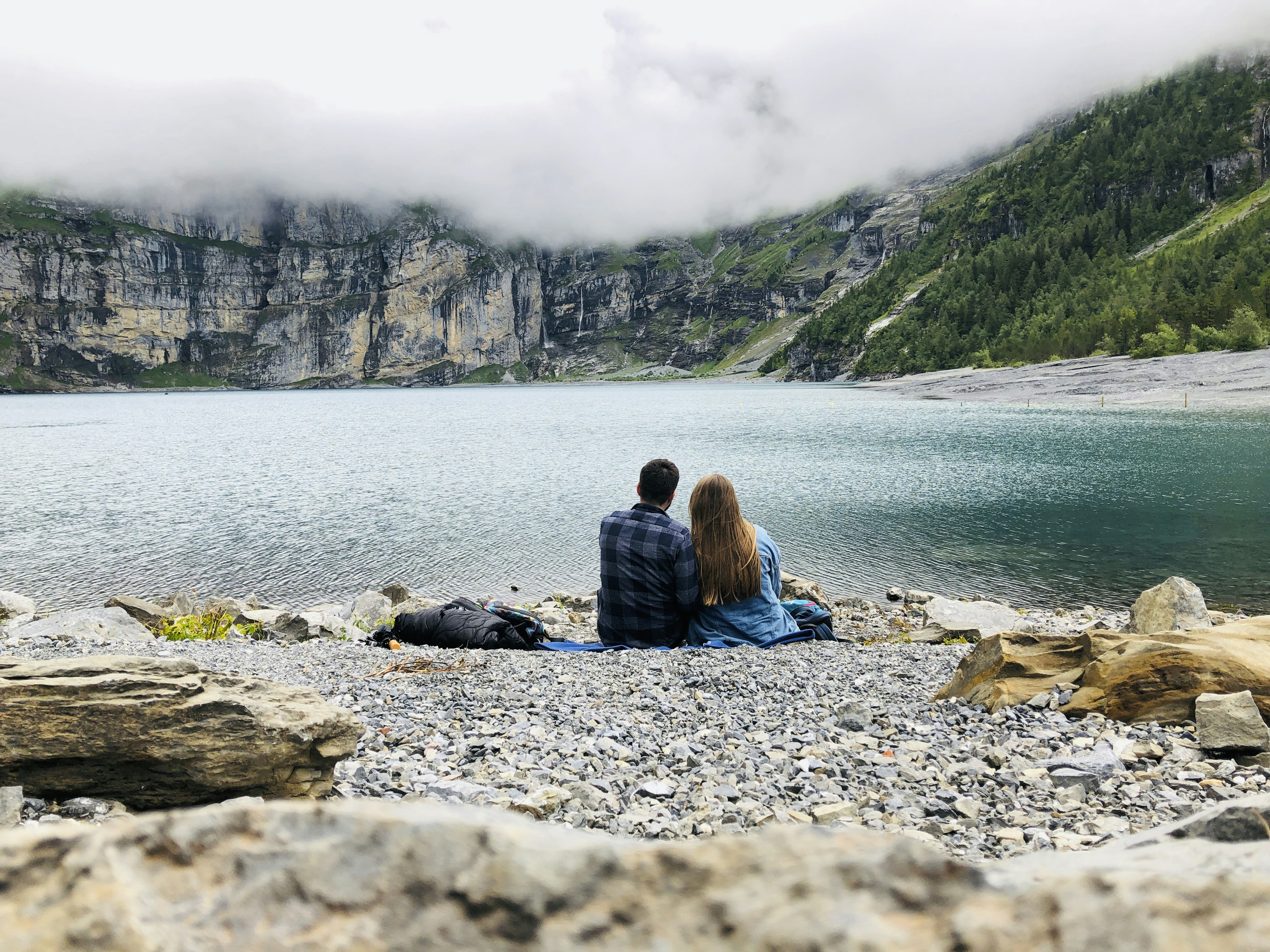 woman in black jacket sitting on rock near body of water during daytime