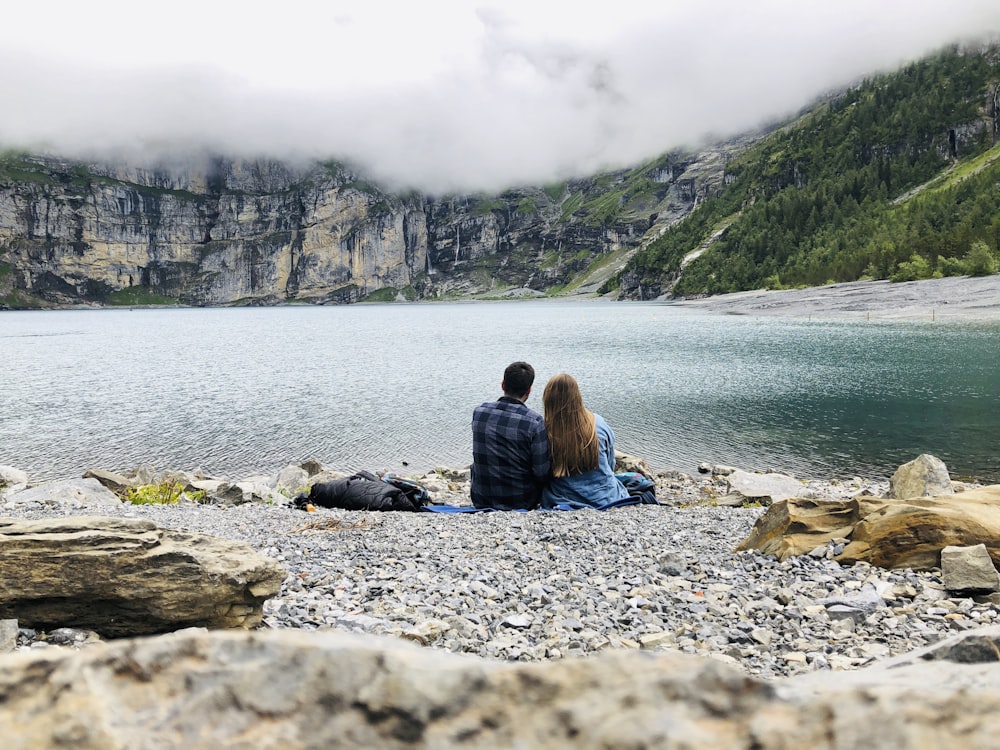 woman in black jacket sitting on rock near body of water during daytime