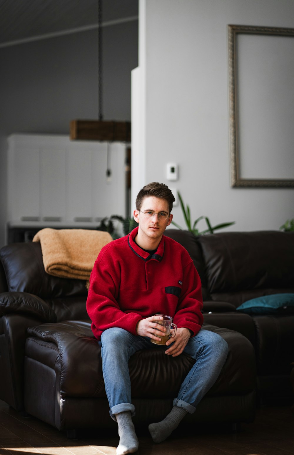 man in red sweater and blue denim jeans sitting on black couch